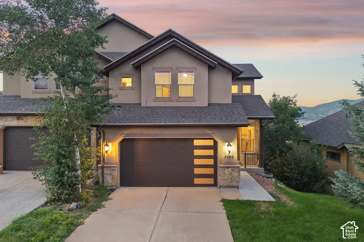 Multi-level exterior featuring stucco siding, stone veneer accents, an asphalt shingle roof, and a contemporary garage door with horizontal glass panels