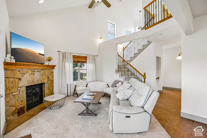Vaulted ceilings featuring a floor-to-ceiling stone fireplace, staircase with wood handrails and iron balusters, and tile flooring