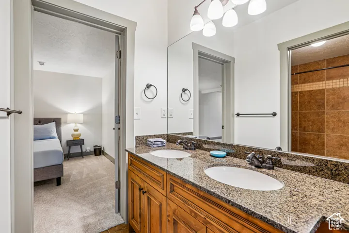 Dual-sink vanity with stone countertop, drop-in basins, dark metal fixtures, and full-width vanity mirror