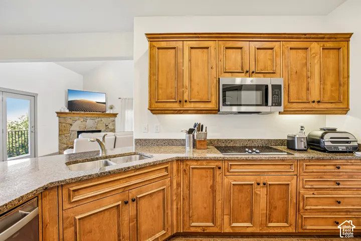 Kitchen featuring stained wood cabinetry, stone countertops, double-basin stainless steel sink, built-in microwave, and flat-surface cooktop