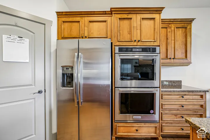 Custom stained wood cabinetry, stainless steel double wall oven, side-by-side stainless steel refrigerator, and stone-finish countertops