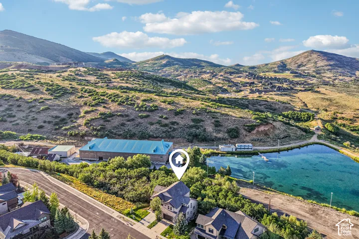 Aerial perspective featuring a multi-story residence with a multi-gabled roofline, situated on a lot with mature trees and a nearby reservoir, set against a mountainous landscape
