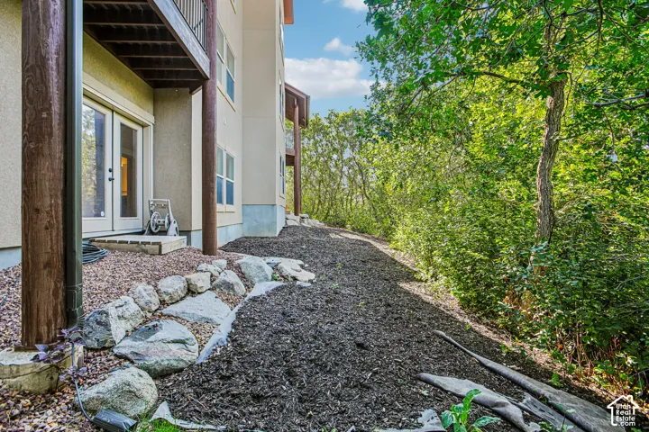 Exterior elevation featuring stucco siding, double glass-pane doors, stone rock-wall landscaping, and mulched ground covering