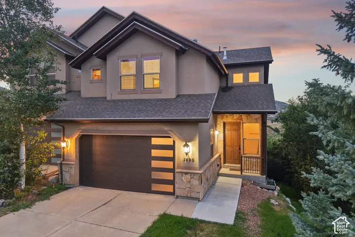 Multi-level exterior featuring stucco siding, stone veneer accents, a dark-toned multi-panel garage door with horizontal glass inserts, and shingle roofing