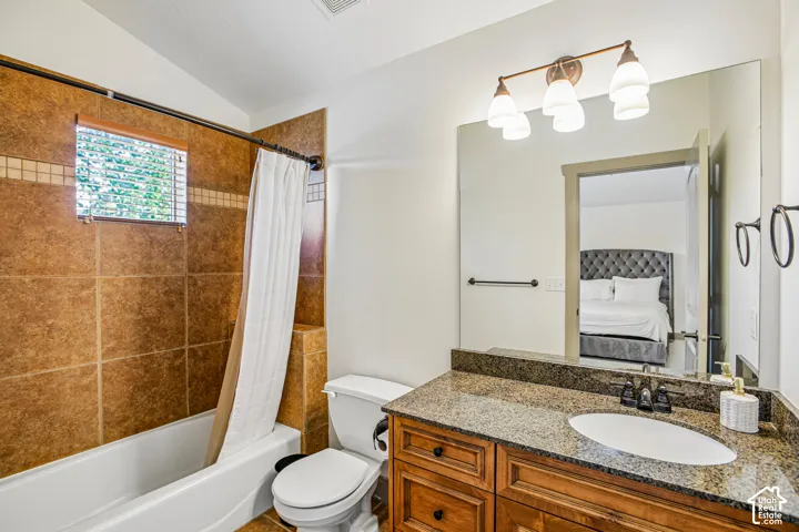 Bathroom featuring an integrated vanity with a stone countertop, an oval under-mount sink, wood-finish cabinetry, a large wall-mounted mirror, and a tile-surround bathtub
