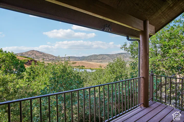Covered deck featuring wood decking, log structural supports, metal railing, and expansive mountain and pond scenery