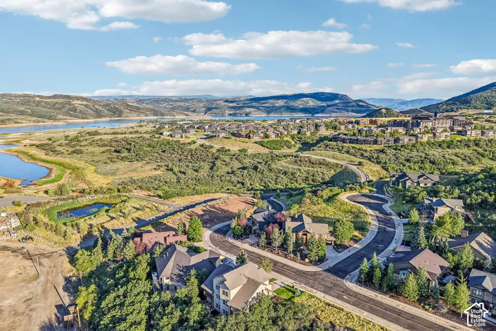 Aerial perspective of a hillside residential community featuring paved cul-de-sacs, native terrain, proximity to a large body of water, and surrounding mountain silhouettes