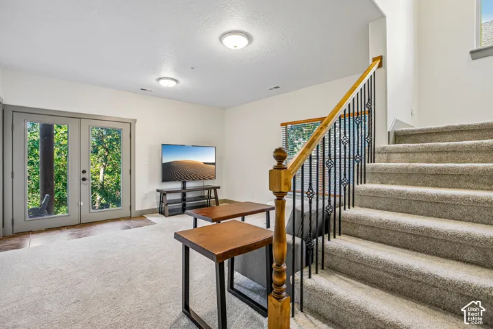 Carpeted interior featuring glass-paneled double doors, staircase with a wood handrail, and decorative metal balusters