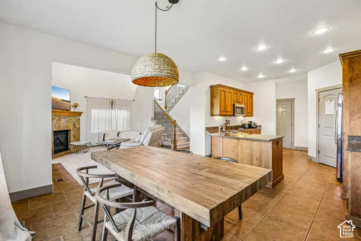 Open-concept interior featuring tile flooring, wood cabinetry, a stone-faced fireplace, recessed lighting, and a woven pendant light fixture