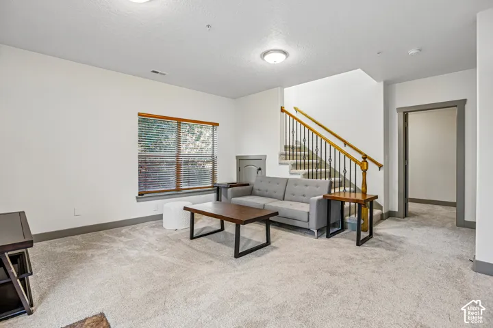 Living space featuring neutral carpeting, a staircase with iron balusters and wood handrail, and trim finished in a dark neutral tone