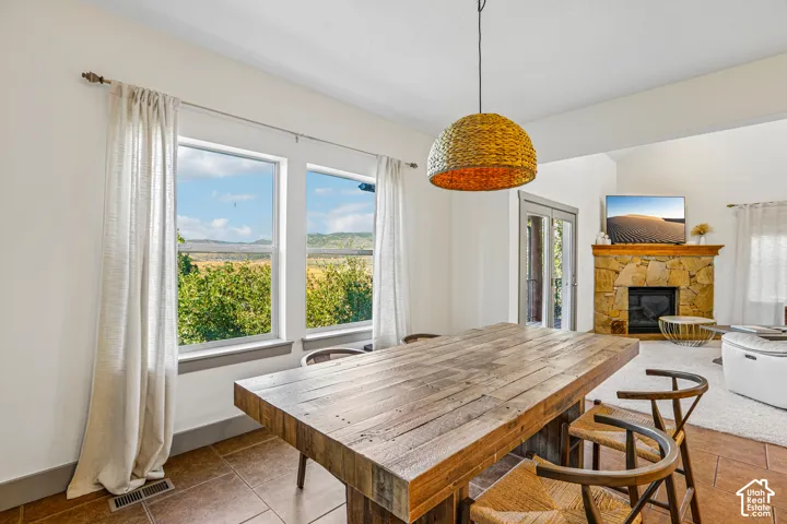Stone-faced fireplace, tile flooring, large windows with natural scenery, and dome-shaped woven pendant lighting