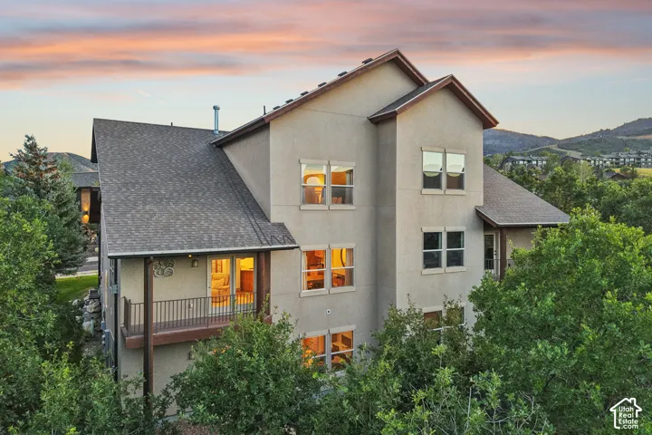 Multi-story residence featuring a textured stucco exterior, architectural shingle roofing, and an integrated balcony with metal railings