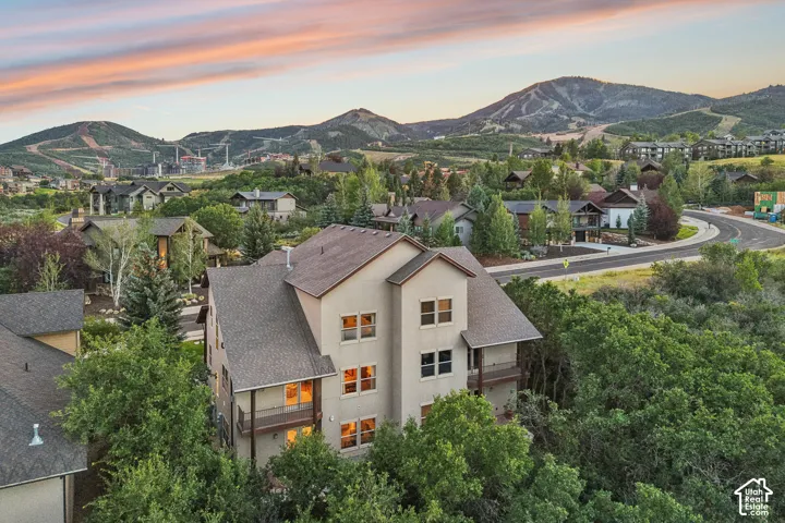 Multi-story residence featuring a shingled roof, neutral-toned siding, tiered balconies, and established surrounding greenery against a mountainous backdrop