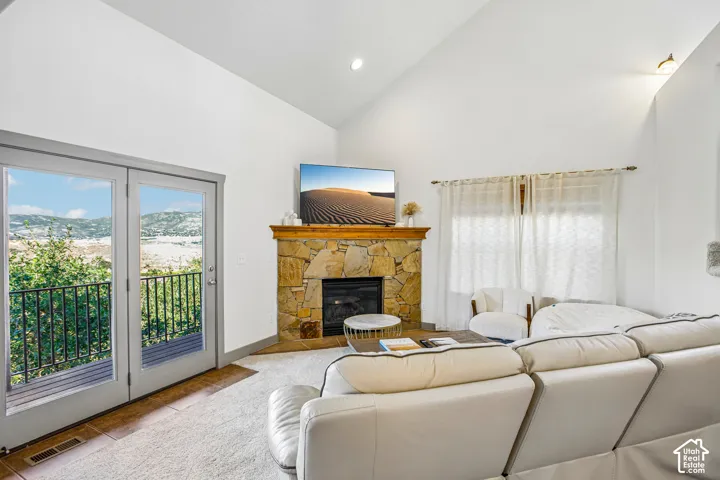 Vaulted ceilings, stone-surround fireplace with a timber mantel, double French doors, and natural scenery backdrop