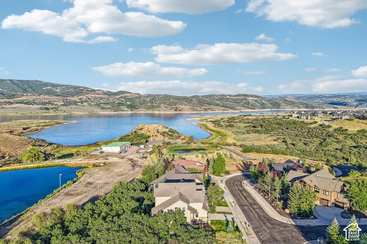 Aerial perspective of a multi-structure residential setting featuring a large body of water, prominent mountain ranges, extensive natural landscaping, and paved streets