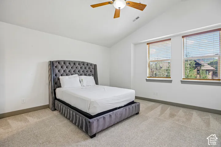 Vaulted ceilings, neutral carpeting, and large windows with horizontal blinds featuring a ceiling-mounted light fixture