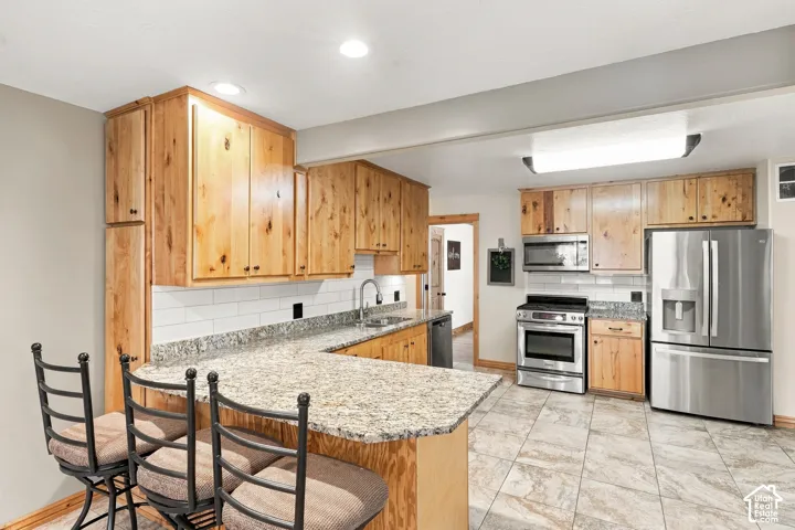 Kitchen featuring natural wood cabinetry, stone-surface countertops, subway tile backsplash, stainless steel appliances, and tile flooring