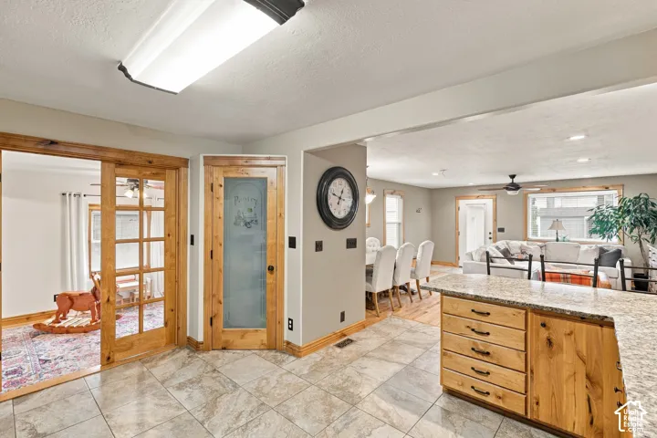 Kitchen featuring custom natural wood cabinetry, stone-finish countertops, tiled flooring, wood-framed French doors, and a decorative pantry door with glass inlay