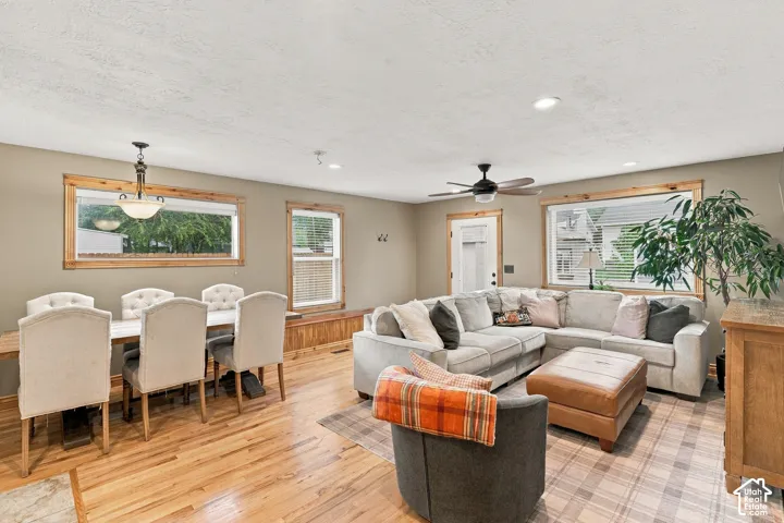Open-concept interior featuring wood-finish flooring, natural wood window trim, a built-in window bench, a multi-blade ceiling fan, and a traditional-style pendant chandelier