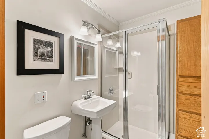 Bathroom featuring a white pedestal sink with chrome faucet, glass-enclosed shower with integrated shelving, built-in wooden cabinetry, and overhead vanity lighting