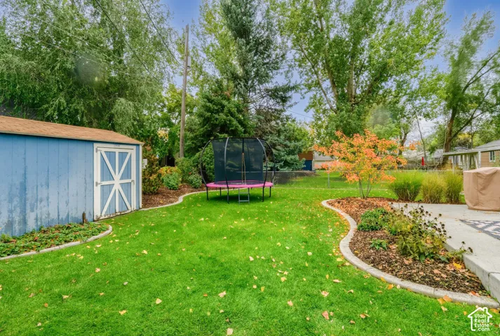 Backyard featuring a manicured lawn, concrete patio, detached storage shed, and established landscaping with concrete curbing