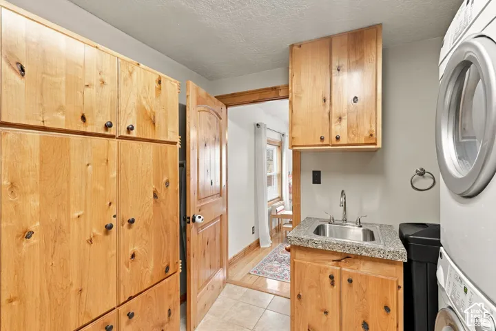 Custom wood-finish cabinetry, stone-composite countertop, stainless steel utility sink, tile flooring, and matching wood-finish paneled door