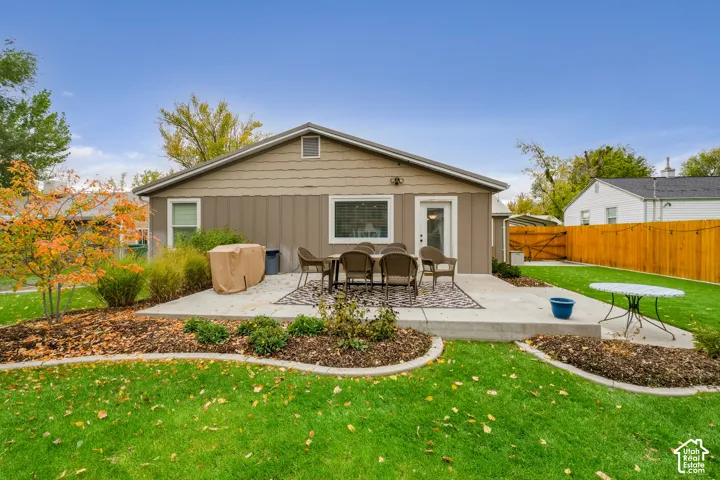 Rear exterior featuring a concrete patio, wood-style siding, manicured lawn, curved landscape beds, and privacy fencing