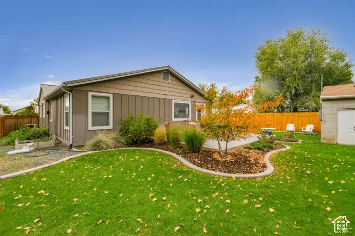 Exterior rear elevation featuring vertical board-and-batten siding, a paved patio, a fenced backyard, and curated garden beds with concrete curbing
