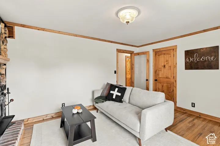 Interior room featuring wood-finish flooring, natural wood crown molding and door trim, a brick fireplace surround, and a central flush-mount ceiling fixture
