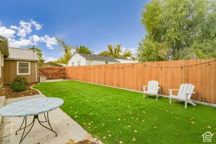 Fenced backyard featuring synthetic turf, concrete patio, and mature trees