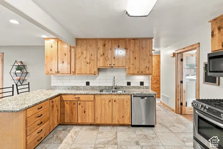 Kitchen featuring knotty wood cabinetry, stone-finish countertops, subway tile backsplash, stainless steel dishwasher, and tile flooring