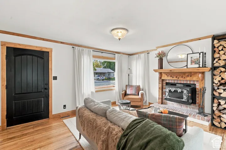 Living area featuring wood-finish flooring, wood-framed entry door, brick-surround fireplace with a wood mantel, built-in firewood storage, and overhead light fixture
