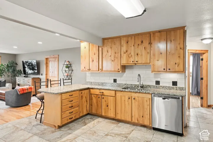 Kitchen featuring natural finish wood cabinetry, stone-patterned countertops, white subway tile backsplash, and stainless steel dishwasher