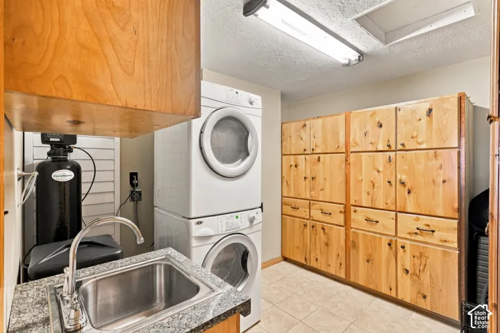 Utility space featuring custom natural-wood cabinetry, stone-finish countertop with an integrated stainless steel sink, tiled flooring, and high-capacity stackable laundry appliances