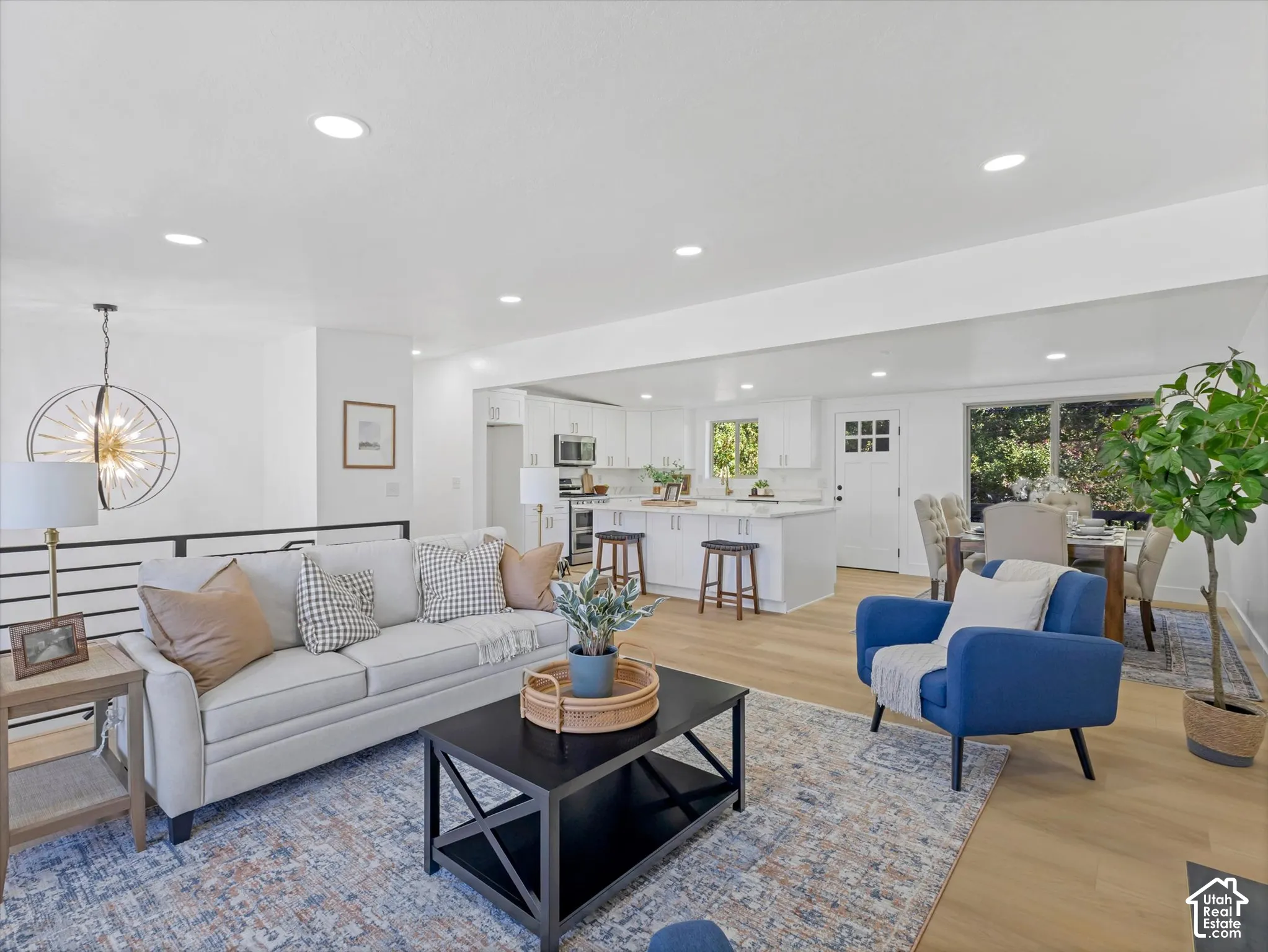 Open concept interior featuring wood-finish flooring, recessed lighting, white cabinetry, a center kitchen island, and a geometric chandelier
