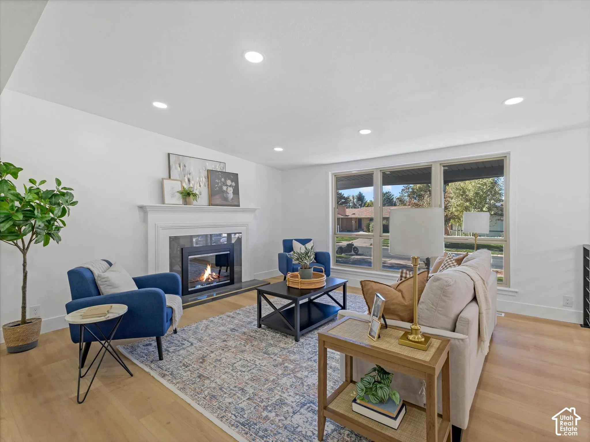 Living area featuring recessed lighting, light-tone wood-finish flooring, and a fireplace with a decorative mantel and stone surround