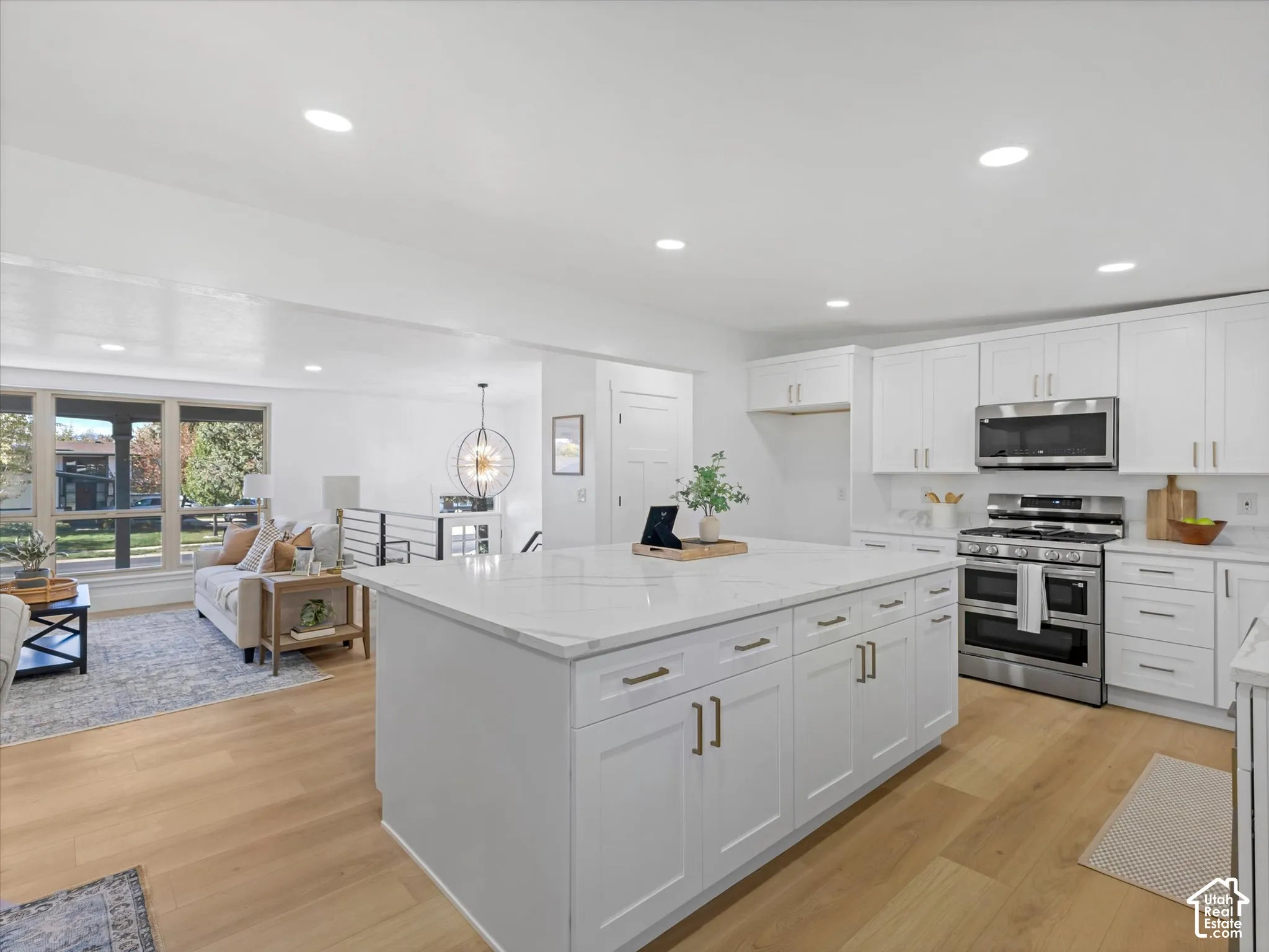 Kitchen featuring white shaker-style cabinetry, a quartz-topped center island with storage, stainless steel appliances, and wood-finish flooring