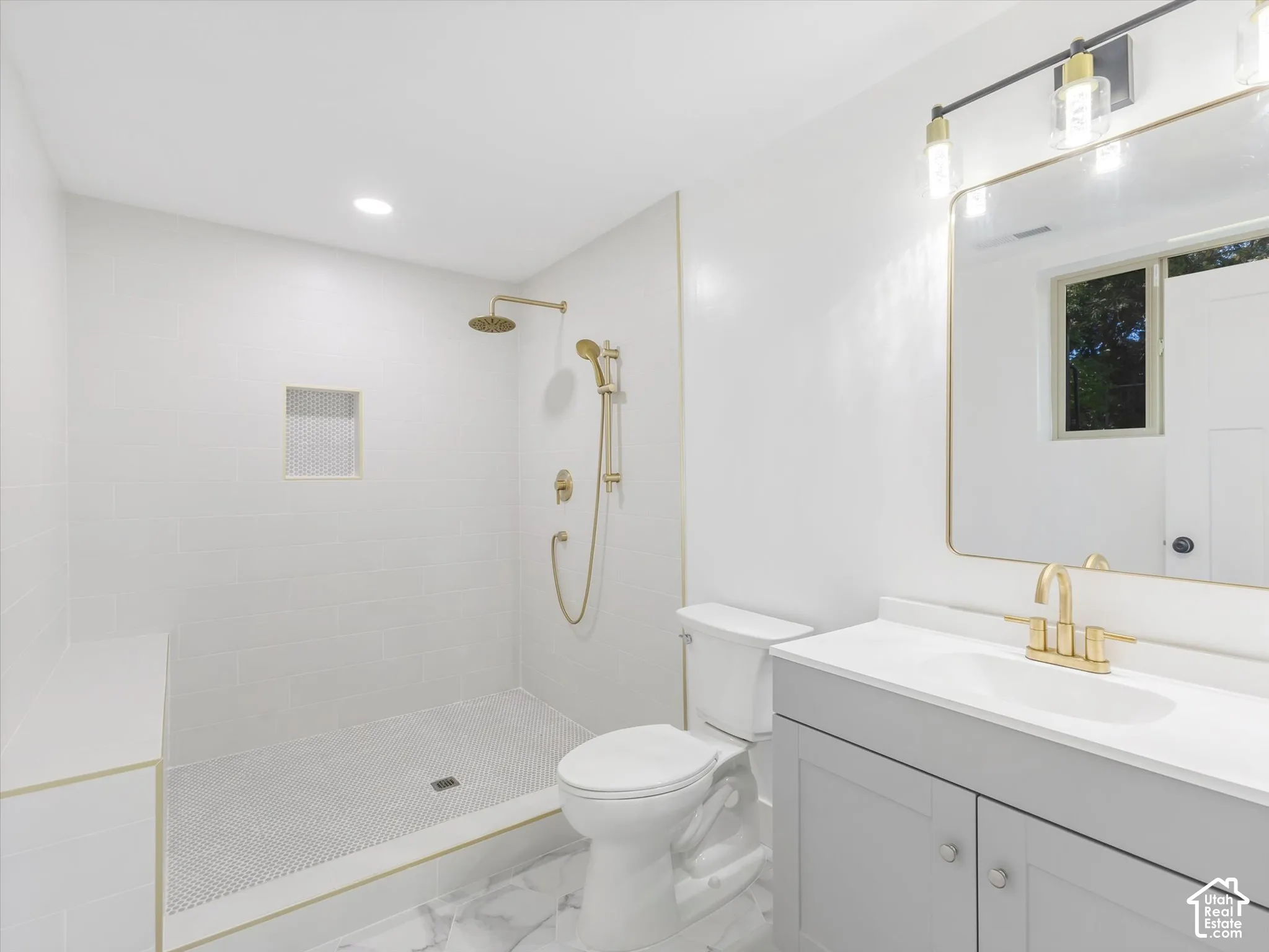 Master Bathroom featuring a walk-in shower with gold-toned rainfall and handheld showerheads, a gray vanity with a white countertop, an integrated sink with gold-toned fixtures, and a wall-mounted mirror