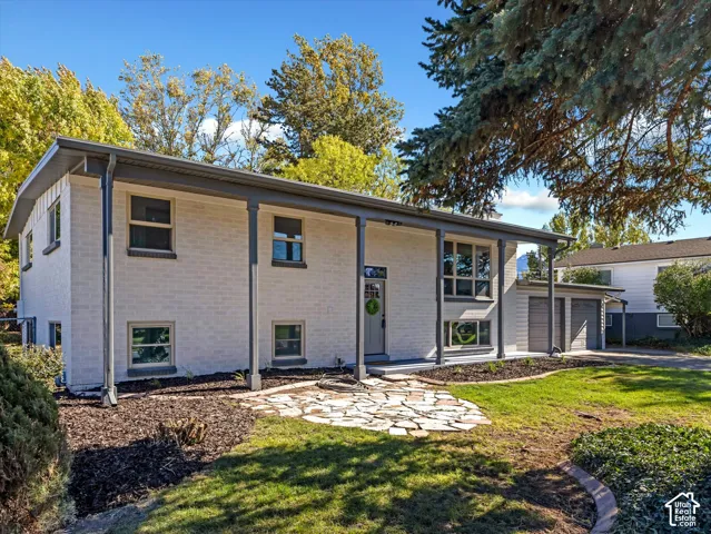 Mid-century modern architectural style featuring painted brick exterior, covered front porch with slender support columns, irregular stone paver walkway, and attached two-car garage