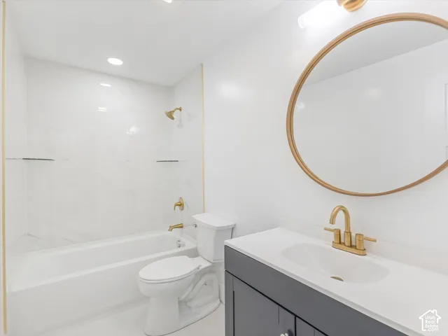 Second Bathroom in basement featuring a dark gray vanity with a white countertop, oval wall-mounted mirror with a gold frame, brass-finish fixtures, and a tub-shower combination with marble-patterned wall surround