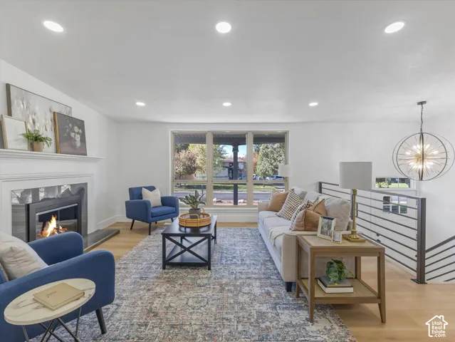 Living area featuring wood-finish flooring, recessed lighting, a fireplace with a white mantel, large picture windows, and an industrial-style metal railing