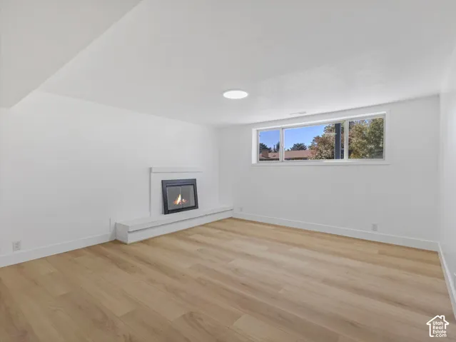 Interior space featuring light wood-finish flooring, a white-framed fireplace with a stepped hearth, a large horizontal window, and a ceiling-mounted skylight