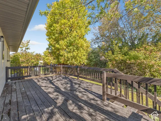 Raised wooden deck featuring dark-stained railings and a staircase leading to the rear grounds, framed by mature trees and foliage