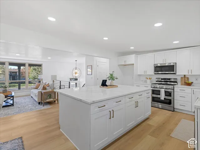 Kitchen featuring white shaker-style cabinetry, a quartz-topped center island with storage, stainless steel appliances, and wood-finish flooring