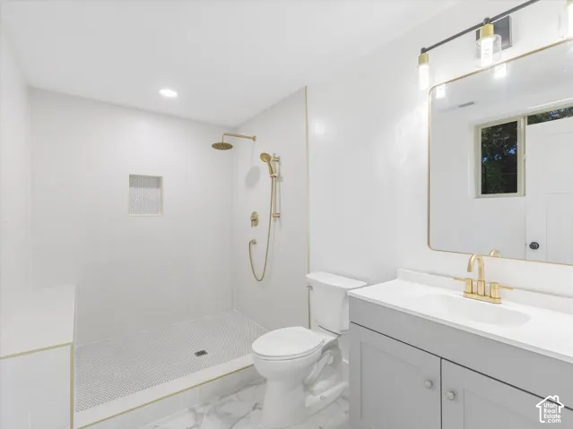 Master Bathroom featuring a walk-in shower with gold-toned rainfall and handheld showerheads, a gray vanity with a white countertop, an integrated sink with gold-toned fixtures, and a wall-mounted mirror