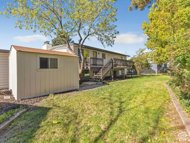 Backyard featuring a raised wooden deck with stairs, a detached storage shed, and mature trees