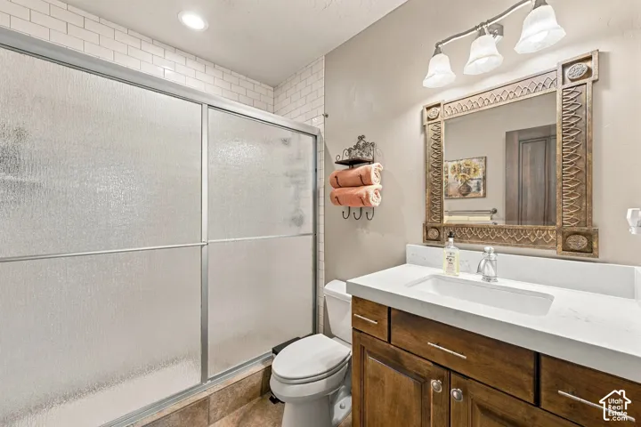 Bathroom featuring a wood-finish vanity with a stone-surface countertop, rectangular undermount sink, tiled shower enclosure with sliding glass doors, and decorative wall-mounted lighting