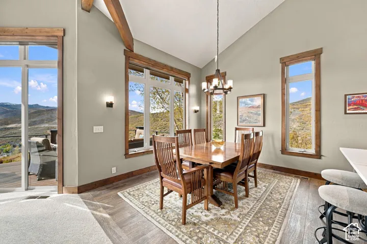 Dining area featuring vaulted ceilings with exposed wood beams, wood-trimmed windows, wood-finish flooring, and a multi-light chandelier