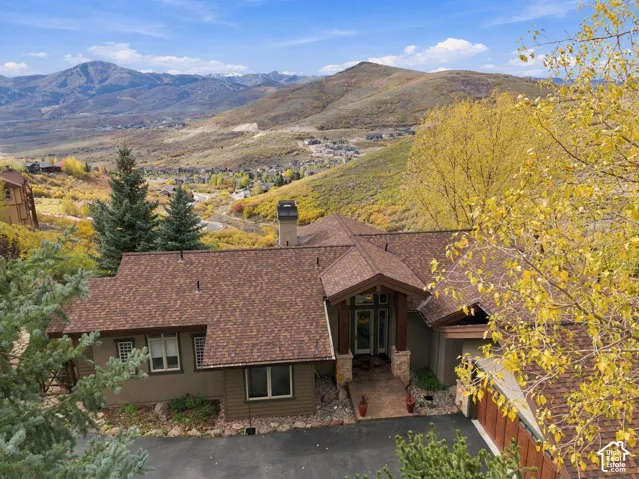 Multi-gabled residence with textured siding, stone exterior accents, asphalt shingled roofing, and mountainous terrain backdrop