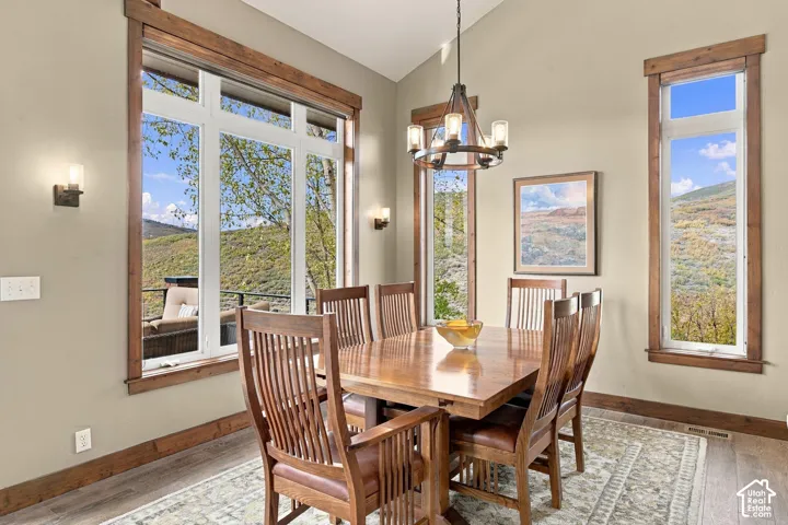 Vaulted ceiling room featuring wood-trimmed windows, a multi-light metal chandelier, and wood-finish flooring